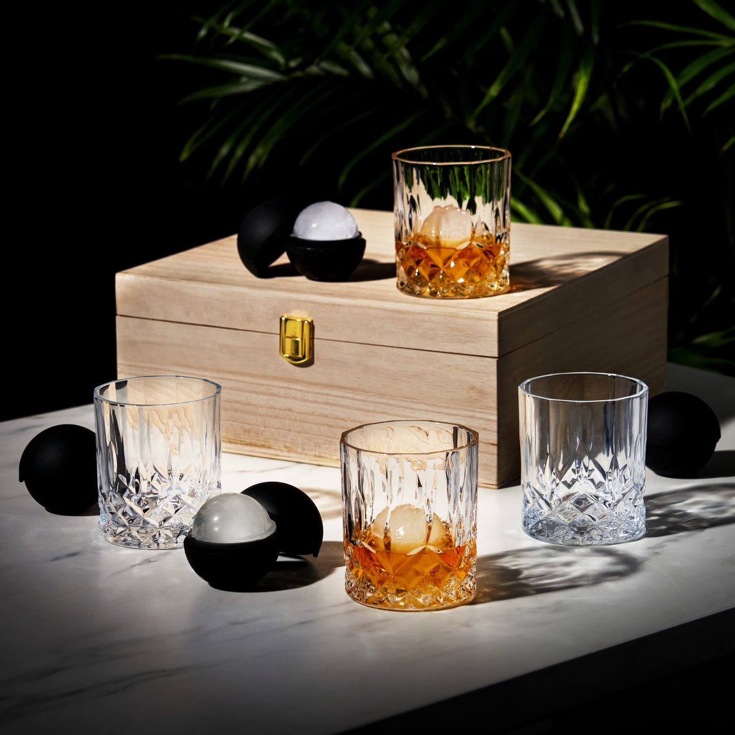 Wooden box with glasses containing a drink and ice cubes on a dark background